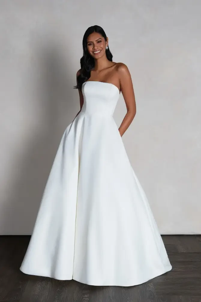 Model is wearing a strapless ball gown with smooth crepe fabric and a minimalist, elegant silhouette.