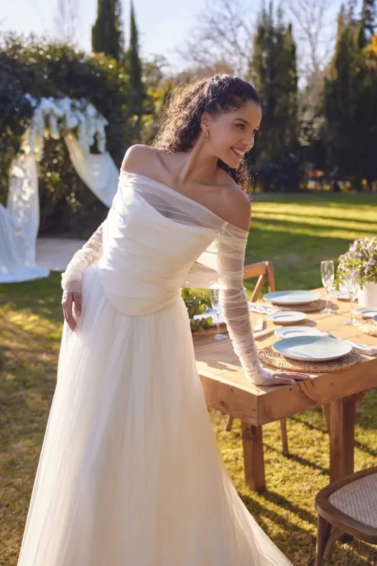 model is wearing an off the shoulder a-line wedding dress with a basque waist