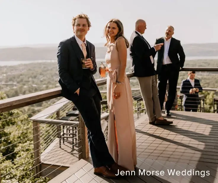 A group of elegantly dressed individuals enjoying a scenic outdoor setting, with one couple posing for the camera.