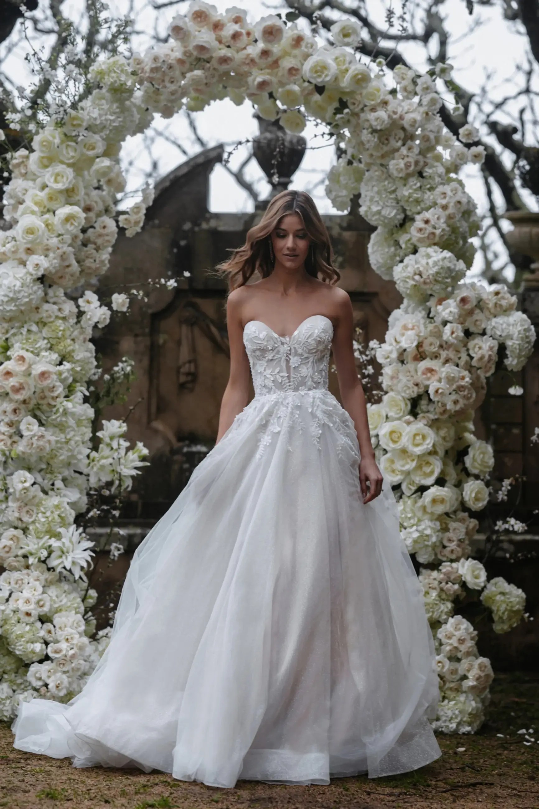 Model is wearing an a-line wedding dress with a tulle skirt and strapless sweetheart bodice